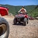 A rider wearing a helmet, goggles and face mask driving in a caravan of all terrain vehicles over mountainous terrain